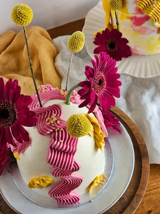 Dome cake decorated with pink and yellow buttercream and fresh flowers