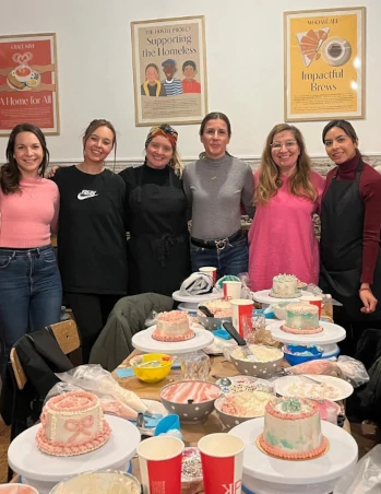 Group of cake workshop participants posing together behind a table with decorated cakes